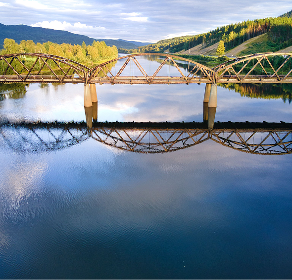 Bridge over calm river with mountain backdrop.
