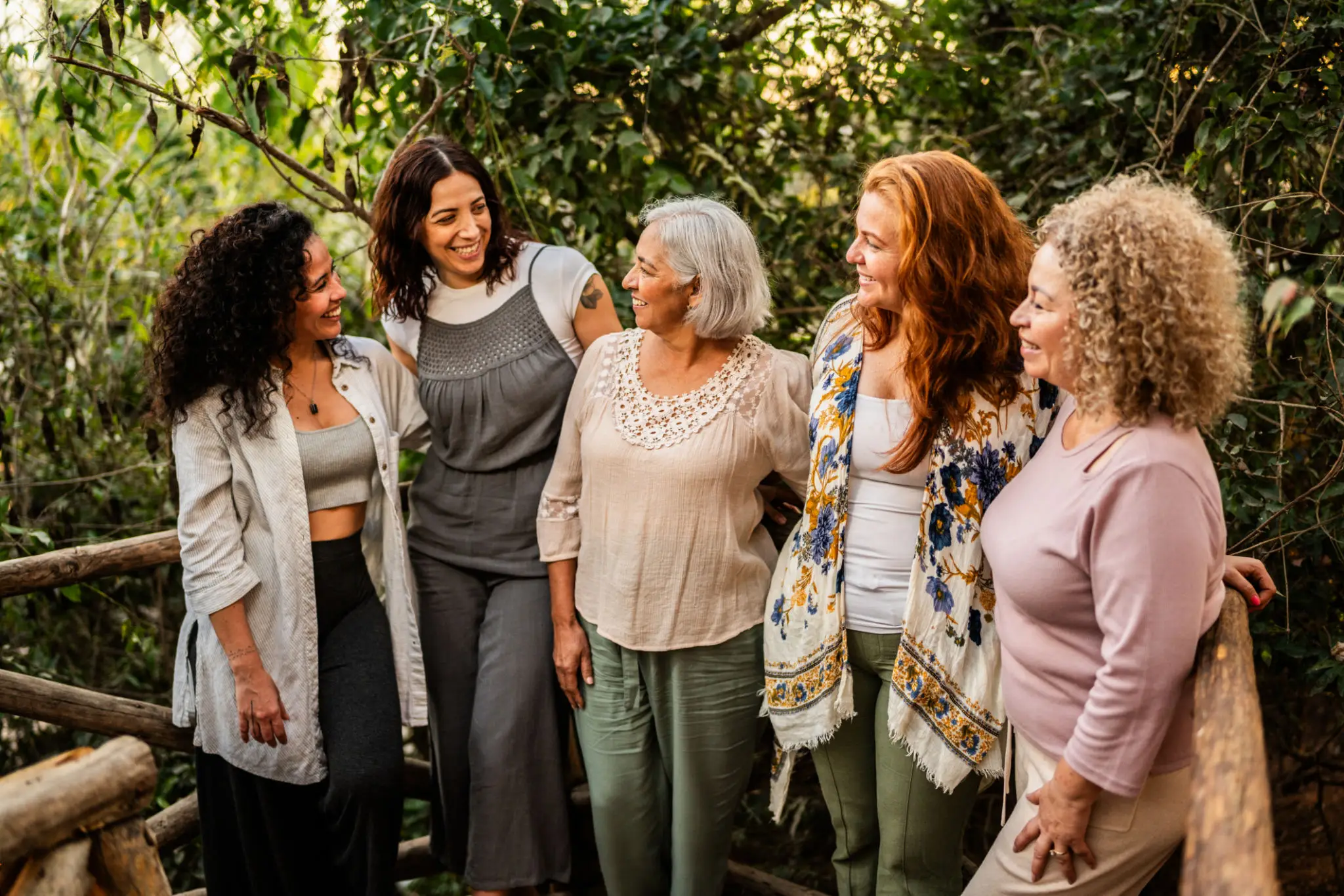 Five women smiling in a wooded area.
